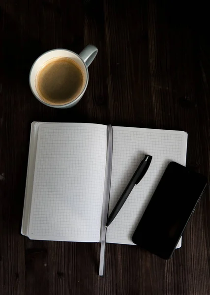Ανοιχτό Λευκό Σημειωματάριο Μαύρο Κινητό Τηλέφωνο Και Ένα Φλιτζάνι Καφέ — Φωτογραφία Αρχείου