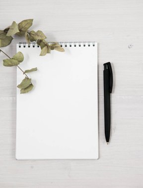 Açık gri tahta masa zemininde, kopya alanı ile beyaz boş not kağıdı ve kalem açılıyor