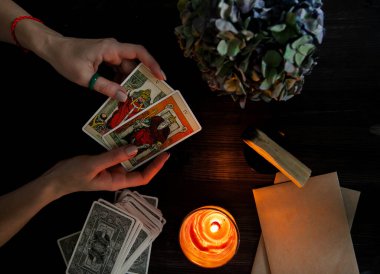  Tarot kartları ellerinde. Karanlık bir arka planda. Mum ışığında.