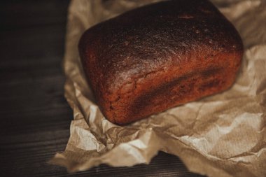 Koyu arka planda ve el işi kağıdında taze pişmiş siyah çavdar ekmeği. Beleş metin alanı olan kasvetli bir arkaplan. en üstteki görünüm
