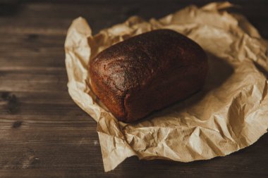 Koyu arka planda ve el işi kağıdında taze pişmiş siyah çavdar ekmeği. Beleş metin alanı olan kasvetli bir arkaplan. en üstteki görünüm