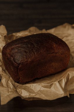 Koyu arka planda ve el işi kağıdında taze pişmiş siyah çavdar ekmeği. Beleş metin alanı olan kasvetli bir arkaplan. en üstteki görünüm