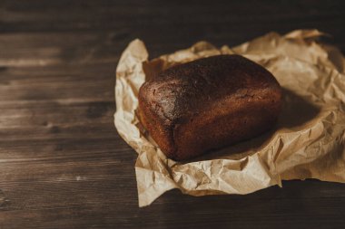 Koyu arka planda ve el işi kağıdında taze pişmiş siyah çavdar ekmeği. Beleş metin alanı olan kasvetli bir arkaplan. en üstteki görünüm
