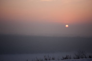 Kırmızı güneş gri-pembe bir sisin içinde batar. Kış pastel manzarası. bal gün batımı