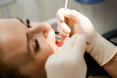 Dişçi genç beyaz bir kadın bir hastayı muayene ediyor. Dişçi koltuğundaki genç beyaz bir kadın.