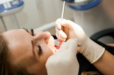 Dişçi genç beyaz bir kadın bir hastayı muayene ediyor. Dişçi koltuğundaki genç beyaz bir kadın.