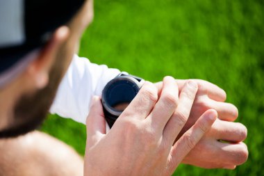 Siyah şortlu ve beyaz gömlekli beyaz bir adam bir spor saate bakar ve ayarlar. Akıllı adam kullanan delikanlıya yakın çekim