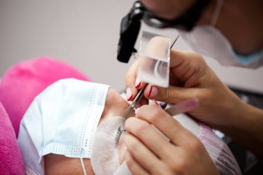 Bir kız, salgın sırasında kirpiklerini uzatma prosedürünü uygular. Elinde aletler olan bir usta.