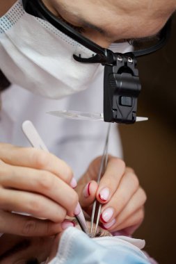 Bir kız, salgın sırasında kirpiklerini uzatma prosedürünü uygular. Elinde aletler olan bir usta.