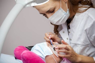 Bir kız, salgın sırasında kirpiklerini uzatma prosedürünü uygular. Elinde aletler olan bir usta.