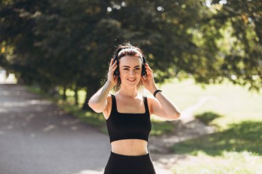 Parkta kulaklıkla koşan atletik, genç ve mutlu bir kadın. Sabahları yaşam tarzı sağlığı için koşuyor. Spor ve sağlıklı aktif yaşam tarzı konsepti. Spor için siyah giysi