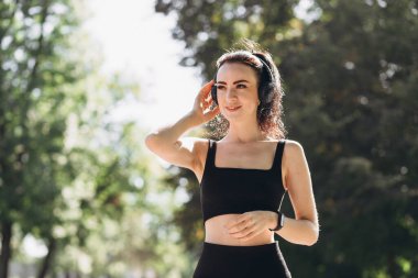 Parkta kulaklıkla koşan atletik, genç ve mutlu bir kadın. Sabahları yaşam tarzı sağlığı için koşuyor. Spor ve sağlıklı aktif yaşam tarzı konsepti. Spor için siyah giysi
