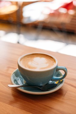 Bir fincan kapuçino, latte sanatıyla birlikte. Kafedeki ahşap masada mavi bardakta kahve. Kolay kahvaltı kavramı.