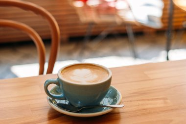 Bir fincan kapuçino, latte sanatıyla birlikte. Kafedeki ahşap masada mavi bardakta kahve. Kolay kahvaltı kavramı.
