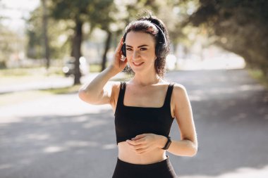 Parkta kulaklıkla koşan atletik, genç ve mutlu bir kadın. Sabahları yaşam tarzı sağlığı için koşuyor. Spor ve sağlıklı aktif yaşam tarzı konsepti. Spor için siyah giysi