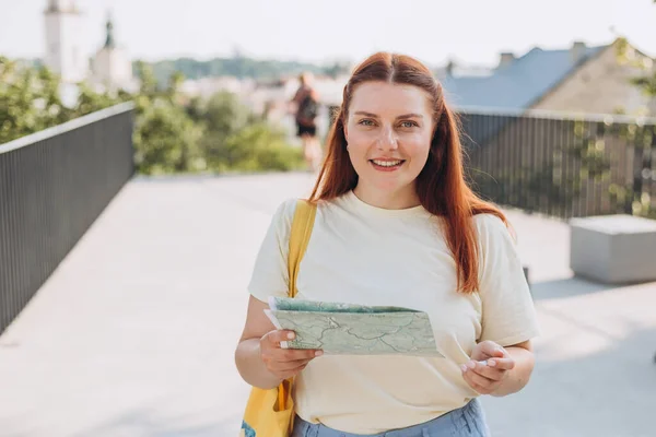 Atraktivní mladá turistka zkoumá nové město. Šťastná zrzka Žena s mapou v rukou — Stock fotografie