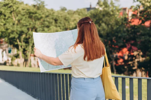 Atraktivní mladá turistka zkoumá nové město. Šťastná zrzka Žena s mapou v rukou — Stock fotografie