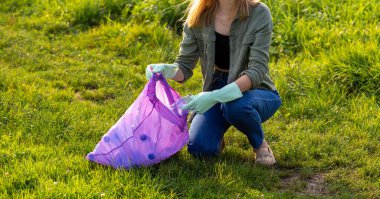 Banner gönüllü elleri plastik çöpleri topluyor. Parktaki çimlerin üzerinde plastik şişe toplayan bir kadın. Küresel çevre kirliliği sorunu. Çevre dostu. Bastır yeşil