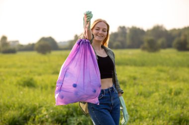 Banner gönüllü elleri plastik çöpleri topluyor. Parktaki çimlerin üzerinde plastik şişe toplayan bir kadın. Küresel çevre kirliliği sorunu. Çevre dostu. Bastır yeşil