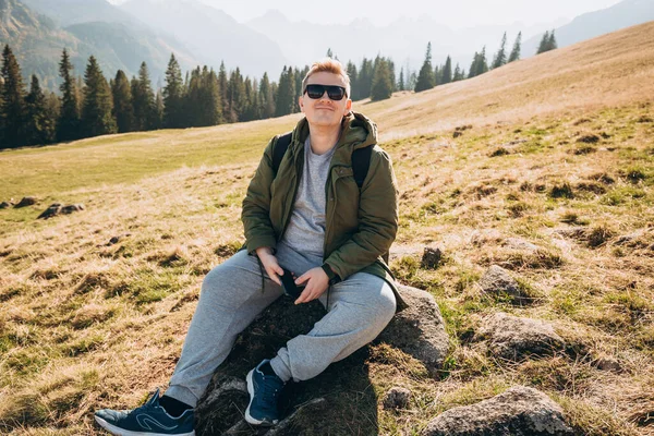 Retrato de hombre positivo en gafas de sol utilizar el teléfono inteligente sobre el fondo de la naturaleza. Picos de montaña. Concepto libertad, felicidad, viajes y vacaciones, actividades al aire libre — Foto de Stock