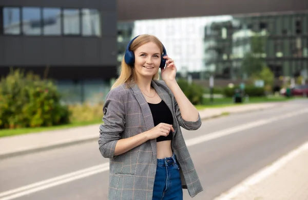 Portrét mladé šťastné ženy poslouchající hudbu se sluchátky a usmívající se při procházce po ulici ve městě. Milovník hudby má rád hudbu. Portrét obchodnice kráčející a usmívající se venku — Stock fotografie