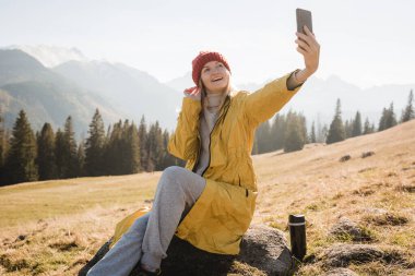 Kar dağlarında fotoğraf çeken genç bir kadın manzaranın tadını çıkarıyor. Özgürlük, mutluluk, seyahat ve tatil konsepti, açık hava aktiviteleri