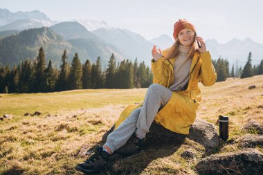 Genç sarışın kadın dağlarda akıllı telefon başında oturuyor ve konuşuyor. Özgürlük, mutluluk, seyahat ve tatil konsepti, açık hava aktiviteleri