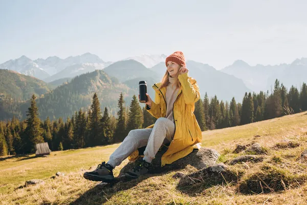 Ταξιδιώτισσα κοπέλα πίνοντας τσάι από θερμός πάνω από το φόντο της φύσης. Βουνό. Ελευθερία, ευτυχία, ταξίδια και διακοπές έννοια, υπαίθριες δραστηριότητες, γυναίκα φορώντας κόκκινο καπέλο — Φωτογραφία Αρχείου