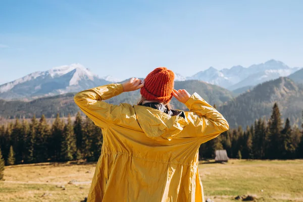 Ευτυχισμένη ξανθιά γυναίκα με κόκκινο καπέλο να στέκεται πίσω και να κοιτάει αλλού. Ταξιδεύει στα βουνά. Ελευθερία, ευτυχία, ταξίδια και διακοπές έννοια, υπαίθριες δραστηριότητες. — Φωτογραφία Αρχείου