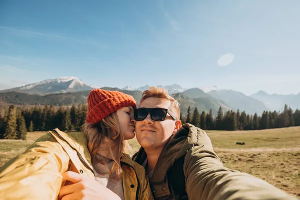 Coppia fare foto selfie in alto nelle montagne di neve godendo la vista. Libertà, felicità, concetto di viaggio e vacanze, attività all'aria aperta, indossa un cappello rosso e lui una giacca verde — Foto Stock