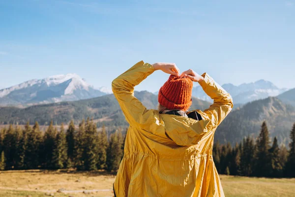 자연의 녹색 배경에서 심장 모양을 보이는 여성. 빨간 모자와 노란 자켓을 입은 행복 한 소녀. 자유, 행복, 여행 및 휴가 개념, 옥외 활동 — 스톡 사진