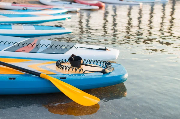 Giallo Paddle board e tavole da surf su sfondo blu superficie dell'acqua pulita. Attrezzature per surf e SUP nelle luci del tramonto primo piano. Sport acquatici all'aperto. Surf concetto di stile di vita. — Foto Stock