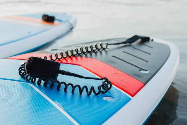 Surf boards op blauw schoon water oppervlak achtergrond. Surfen en SUP boarding apparatuur in zonsondergang verlichting close-up. Buitenwatersporten. Surfen lifestyle concept. — Stockfoto