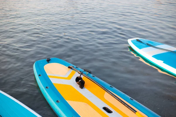 Pranchas de surf em azul fundo superfície de água limpa. Surf e SUP equipamento de embarque em luzes de pôr do sol close-up. Esportes aquáticos ao ar livre. Conceito de estilo de vida surf. — Fotografia de Stock