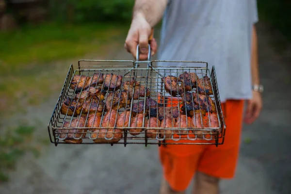 Hombre sosteniendo una parrilla con carne. Descansa en el campo afuera. Barbacoa Grill Street Food. Cocina barbacoa de verano, picnic divertido. —  Fotos de Stock