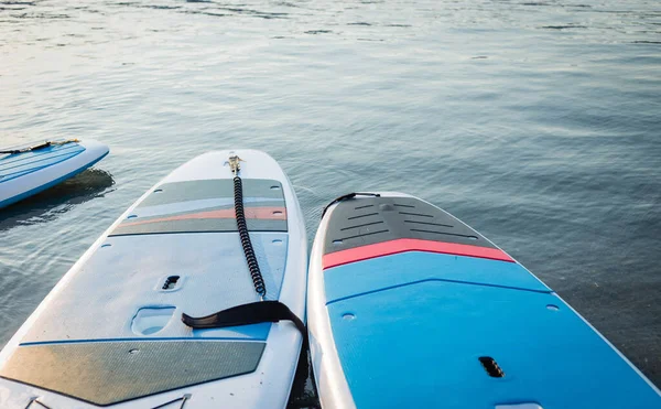 Surf boards op blauw schoon water oppervlak achtergrond. Surfen en SUP boarding apparatuur in zonsondergang verlichting close-up. Buitenwatersporten. Surfen lifestyle concept. — Stockfoto