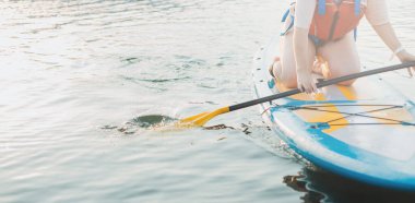 Happy woman studing on paddle board at sunset. Outdoor water sports. Rent of equipment for swimming in the ocean or sea
