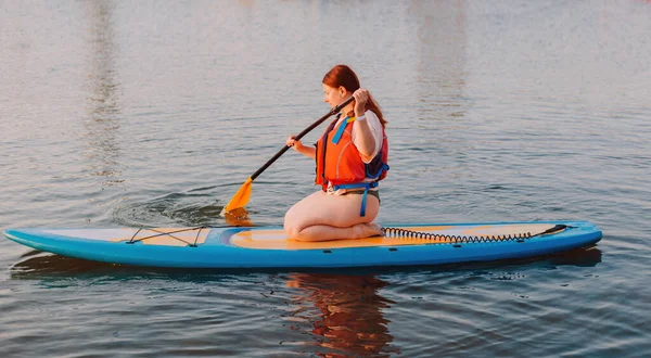 Happy woman studing on paddle board at sunset. Outdoor water sports. Rent of equipment for swimming in the ocean or sea — Stock Fotó