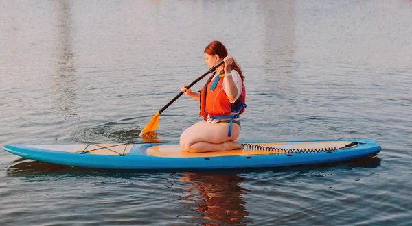 Happy woman studing on paddle board at sunset. Outdoor water sports. Rent of equipment for swimming in the ocean or sea — Stok fotoğraf