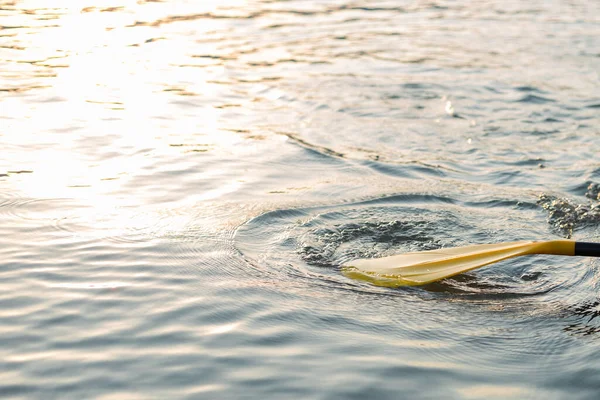 Yellow Paddle board on blue clean water surface background. Surfing and SUP boarding equipment in sunset lights close-up. Outdoor water sports. Rent of equipment for swimming in the ocean or sea — Stock Fotó