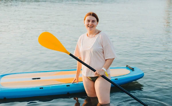 Ευτυχισμένη γυναίκα που καρφώνει με κουπί στο ηλιοβασίλεμα. Υπαίθρια θαλάσσια σπορ. Ενοικίαση εξοπλισμού για κολύμπι στον ωκεανό ή στη θάλασσα — Φωτογραφία Αρχείου