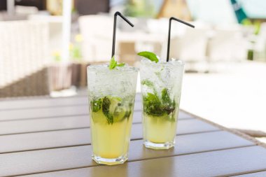 İki bardak limonata ya da naneli mojito kokteyli, serin, ferahlatıcı içecek ya da içecek, açık havada. Buzlu ve samanlı soğuk detoks suyu, boşluğu kopyala.