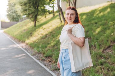 Elinde beyaz pamuk torbayla mutlu genç bir kadın. Model ve sıfır atık konsepti. Eko Doğa Dostane Tarzı. Çevresel Koruma Geri Dönüşümü maketi