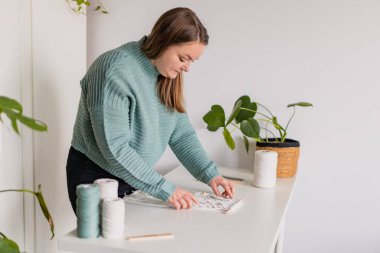 Evinde makrome işi yapan bir kadın. Doğal pamuk iplikler ve tahta boncuklar. El yapımı makrome kemer. Kadın hobisi.