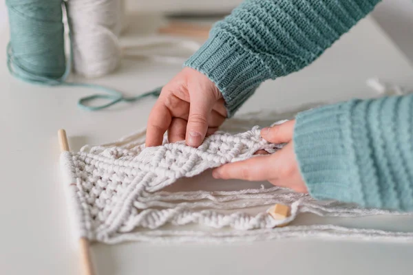 Hand van een vrouw als ze macrame maakt. Natuurlijke katoenen draden en houten kralen. Handgemaakte macrame riem in het werkproces. Vrouwelijke hobby. — Stockfoto