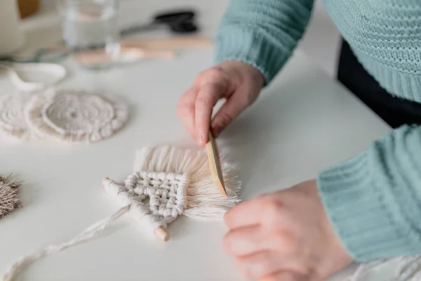 Vrouw die de laatste details van een bijna afgewerkt macramestuk uitwerkt, touwen uitkamt in een huiskamer. Sluit maar af. Natuurlijke katoenen draden en houten kralen. Vrouwelijke hobby. Wanddecoratie. — Stockfoto