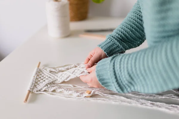 Hand van een vrouw als ze macrame maakt. Natuurlijke katoenen draden en houten kralen. Handgemaakte macrame riem in het werkproces. Vrouwelijke hobby. — Stockfoto