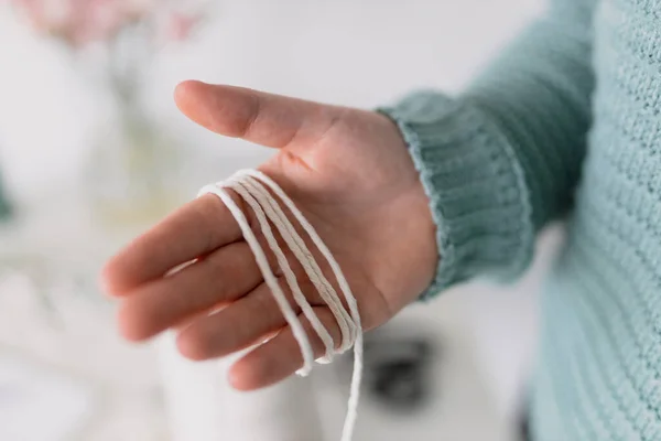 Φυσικό ανακυκλωμένο βαμβακερό σχοινί στο χέρι των γυναικών. Το χέρι μιας γυναίκας όταν φτιάχνει μακαρόνια. Φυσικά βαμβακερά νήματα. Χειροποίητη ζώνη μακραμέ στη διαδικασία της εργασίας. Γυναικείο χόμπι. — Φωτογραφία Αρχείου