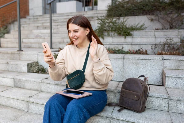 Hermosa estudiante sonriente haciendo una selfie con teléfono inteligente al aire libre. Comunicación telefónica. Feliz joven alegre caminando por la calle de la ciudad, concepto de estilo de vida urbano. Viajero — Foto de Stock