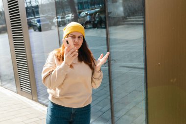 Yakından bakınca üzgün, şüpheci, mutsuz, ciddi bir kadın açık havada telefon ekranına bakıyor. Negatif insani duygu yüz ifadesi hissi, yaşam reaksiyonu. Kötü haber.